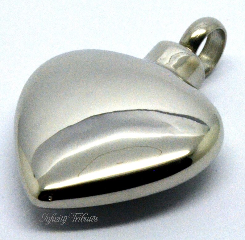 May include: A silver heart-shaped cremation pendant with a screw-on lid. The pendant is made of stainless steel and has a polished finish.