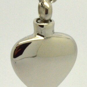 May include: A silver heart-shaped cremation necklace with a chain. The pendant has a screw-on top for filling with ashes.