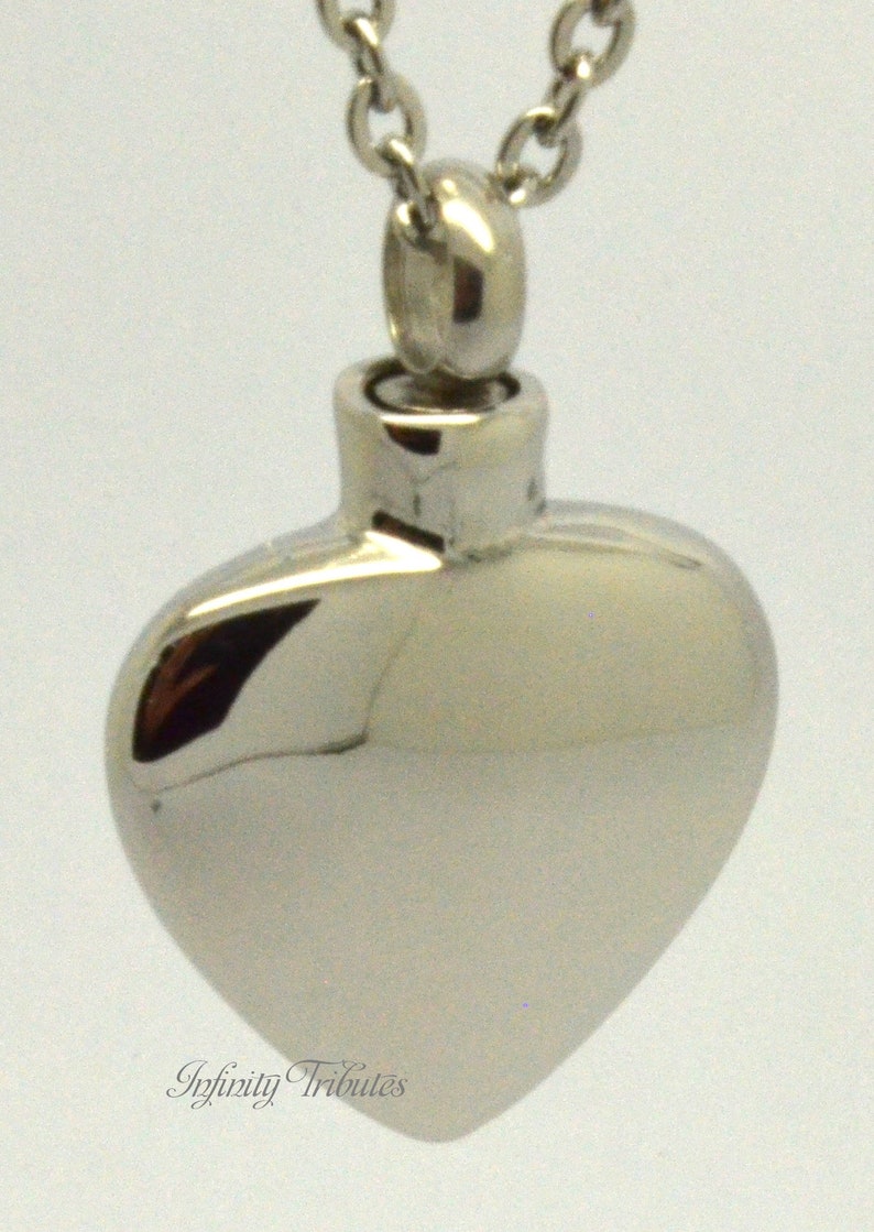 May include: A silver heart-shaped cremation necklace with a chain. The pendant has a screw-on top for filling with ashes.