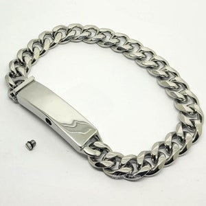 Op de afbeelding: Een zilverkleurige gourmetarmband met een rechthoekige plaat. De armband heeft een gepolijste afwerking en een schroefje ligt naast de plaat. De armband ligt op een witte achtergrond.