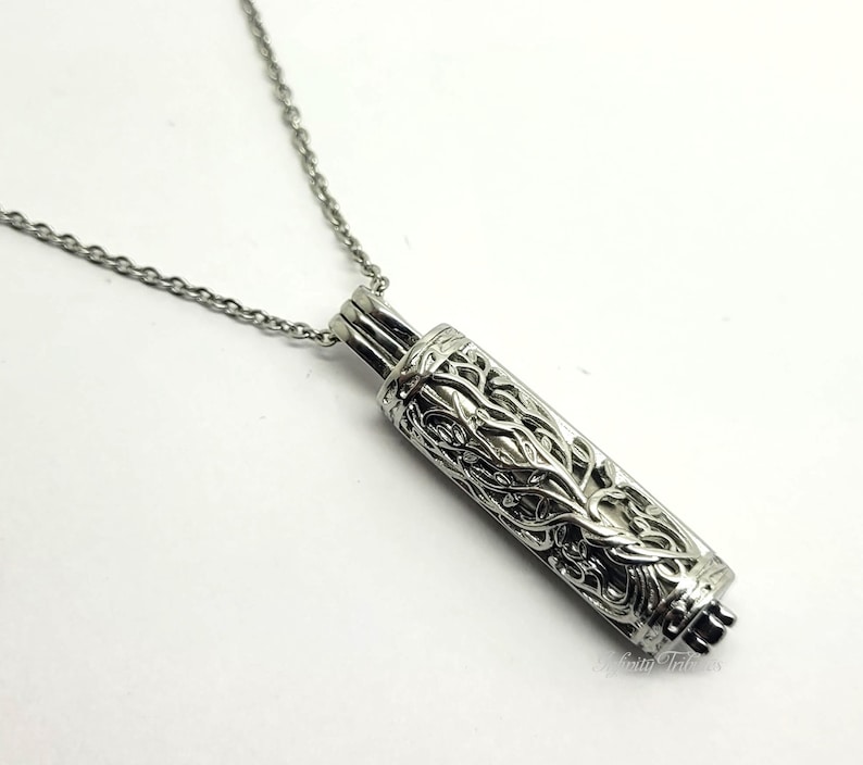 May include: Silver necklace with a detailed, cylindrical pendant featuring a tree of life design.
