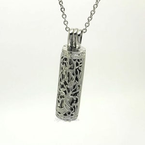 May include: Silver necklace with a delicate, ornate pendant shaped like a cylinder with a floral design. The pendant is open on both ends.