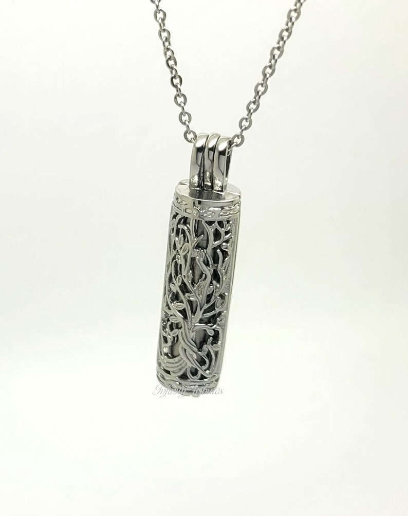 May include: Silver necklace with a delicate, ornate pendant shaped like a cylinder with a floral design. The pendant is open on both ends.