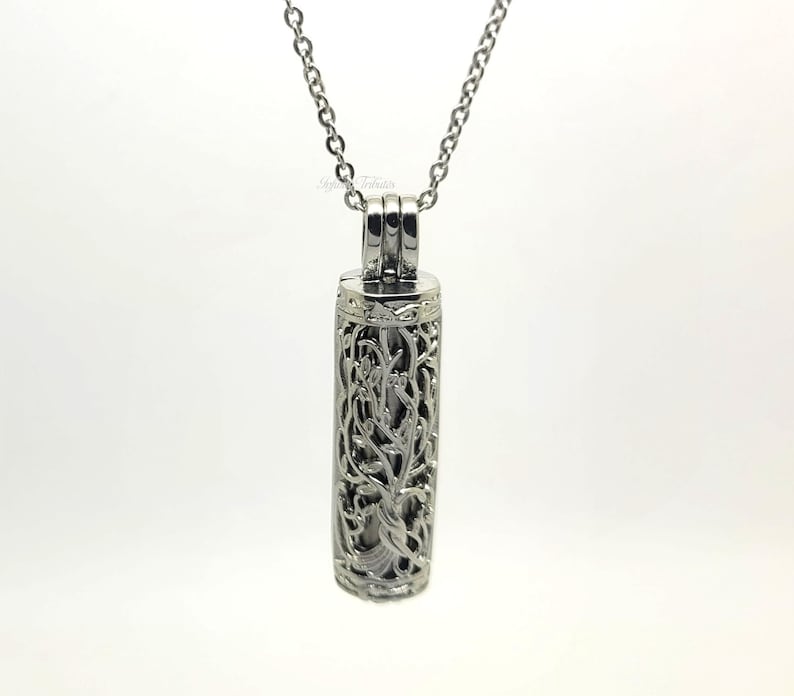 May include: Silver necklace with a delicate, ornate, cylindrical pendant. The pendant is openwork and features a floral design.