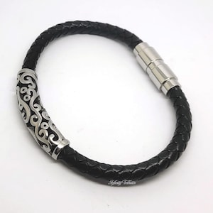 Può includere: Un braccialetto in pelle nera con una chiusura magnetica argentata e un accento decorativo argentato. L'accento presenta un design a spirale.