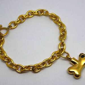 May include: A gold chain bracelet with a gold bone charm. The bone charm has black paw prints on it.