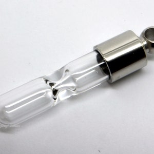 May include: A silver hourglass pendant with a clear glass tube and a silver cap. The pendant has a loop at the top for attaching to a chain.