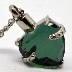 May include: A silver heart-shaped cremation pendant with a green crystal. The pendant is on a silver chain.