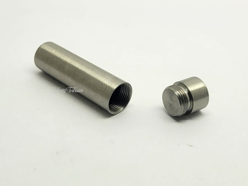 May include: A silver metal tube with a threaded cap. The tube is open at one end and has a threaded opening at the other end.