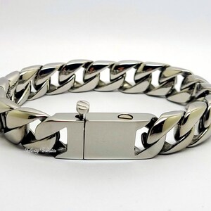 May include: A polished silver-tone curb chain bracelet. The bracelet features a wide, interlocking chain design with a secure clasp. The metal reflects light, creating a bright, shiny appearance. A stylish accessory.