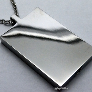 May include: A silver pendant necklace with a rectangular, brushed metal charm. The charm has a smooth, reflective surface.
