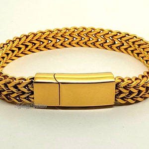 Könnte beinhalten: Ein goldfarbenes Armband mit einem geflochtenen Weizenkettenmuster und einem glatten, rechteckigen Metallverschluss. Das Armband hat eine polierte Oberfläche und ein durchgehendes Gliedermuster. Der Text Infinity Tributes ist sichtbar.
