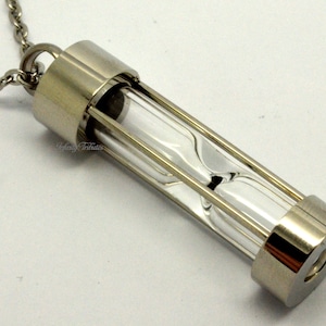 Può includere: Una collana d'argento con un piccolo ciondolo a forma di clessidra. La clessidra è in vetro trasparente e ha una cornice d'argento. La collana è lunga circa 45 cm.