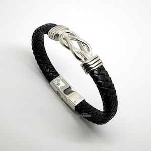 May include: A black leather bracelet with a silver knot clasp. The bracelet is braided and has a silver clasp with a polished finish.