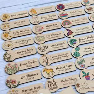 May include: Wooden name tags with various professions and illustrations. The tags feature names like "Mrs. Hawkins" and "Dr. Mainer," along with images of animals, flowers, and other designs. The text "Teach Love Inspire" is also visible.
