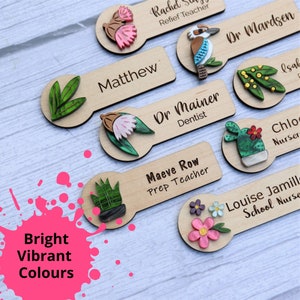 May include: Wooden name tags with colorful illustrations and text. The tags feature a variety of designs, including flowers, plants, a bird, and a cactus. The text on the tags includes names and titles, such as "Matthew", "Dr. Mainer, Dentist", and "Maeve Row, Prep Teacher".