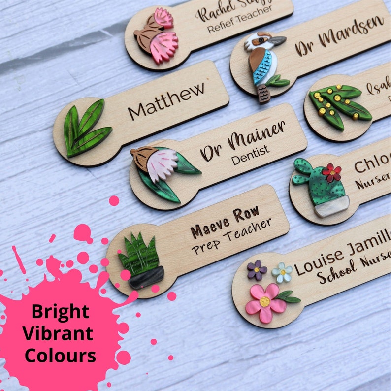 May include: Wooden name tags with colorful illustrations and text. The tags feature a variety of designs, including flowers, plants, a bird, and a cactus. The text on the tags includes names and titles, such as "Matthew", "Dr. Mainer, Dentist", and "Maeve Row, Prep Teacher".