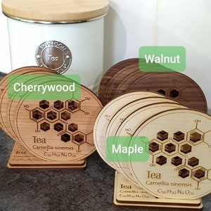 May include: Set of four wooden coasters featuring a chemical structure of tea, with the text "Tea Camellia sinensis C50 H50 N4 O26" and the words "Cherrywood", "Walnut", "Maple" printed on the coasters.