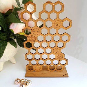 May include: Wooden honeycomb earring stand with a natural wood finish. The stand has 30 holes for earrings and a small bee design on the base.