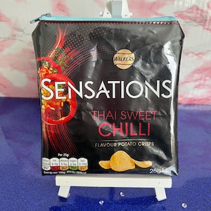 Op de afbeelding: Een zwarte en rode ritszak gemaakt van een gerecyclede Walkers Sensations Thai Sweet Chilli Flavour Potato Crisps zak. De zak heeft een blauwe rits en de voedingsinformatie van de zak is zichtbaar aan de zijkant.