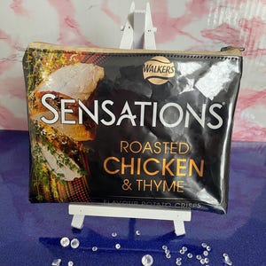 May include: Black zippered pouch with a glossy finish. The pouch features a printed image of a bag of Walkers Sensations Roasted Chicken & Thyme potato crisps.