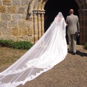 Może przedstawiać: Panna młoda w białej sukni ślubnej z długim welonem idzie do ołtarza w kościele z ojcem.