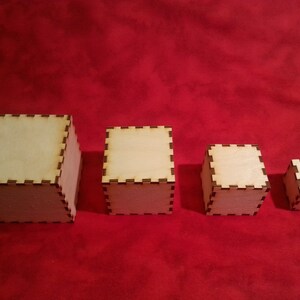 May include: Four wooden boxes of varying sizes, all with a light brown finish and a decorative border. The boxes are arranged in a row from largest to smallest on a red surface.