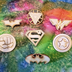 May include: Seven wooden cutouts of popular superhero logos, including Batman, Superman, Wonder Woman, Iron Man, Captain America, and two versions of the Hulk's fist.