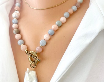 Puede incluir: Un collar delicado con un gran colgante de perla barroca. El collar está hecho de cuentas de colores pastel, incluyendo rosa, azul y verde. El colgante está unido a un cierre de palanca de oro.