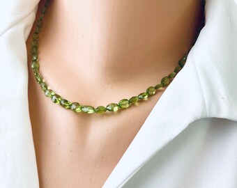May include: A necklace composed of small, faceted, oval-shaped olive green peridot beads strung together in a single strand. The translucent gemstones display a consistent light green hue and are arranged uniformly around the neck area.