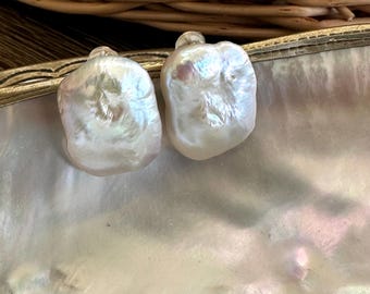 May include: A pair of white baroque pearl earrings with a slightly iridescent sheen. The pearls are irregularly shaped and have a smooth, polished surface.
