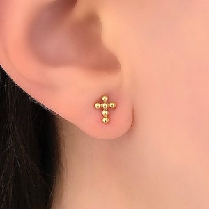 May include: A pair of gold cross stud earrings. The cross is made of small, round beads.