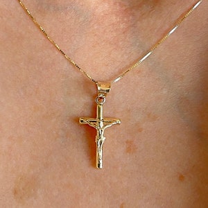 May include: A gold chain necklace with a small gold cross pendant featuring a figure of Jesus Christ.