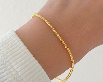 May include: A gold beaded bracelet on a person's wrist.