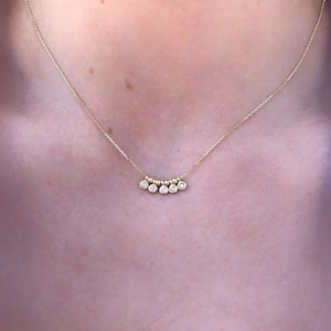 May include: A delicate gold necklace featuring a series of small, sparkling gemstones. The necklace has a fine chain and a pendant with multiple round, clear stones. The design is simple and elegant, suitable for everyday wear or special occasions.