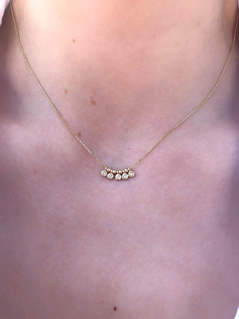 May include: A delicate gold necklace featuring a series of small, sparkling gemstones. The necklace has a fine chain and a pendant with multiple round, clear stones. The design is simple and elegant, suitable for everyday wear or special occasions.