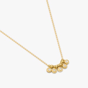 May include: A delicate gold necklace featuring a series of small, round, bezel-set diamonds. The necklace has a fine chain and a cluster of five diamond pendants, with a row of gold beads above them.