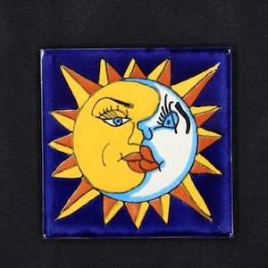 May include: A ceramic tile with a blue background and a yellow sun with a red mouth and blue eyes kissing a white moon with a blue eye and black eyelashes. The sun and moon are surrounded by orange and yellow rays.