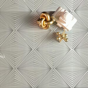 May include: A set of gray ceramic tiles with a geometric pattern. The tiles have a raised, textured design that resembles a sunburst. The tiles are arranged in a grid pattern.