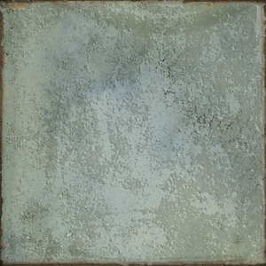 May include: A square ceramic tile featuring a textured, matte surface in shades of pale sage green and muted gray. The finish appears weathered and uneven, with subtle variations in color depth across the face and a dark, rustic brown edge.