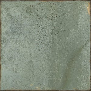 May include: A square ceramic tile with a textured, matte surface in a muted sage green color. The tile features a weathered, uneven finish with subtle variations in tone and a dark, rustic edge that frames the entire perimeter of the piece.
