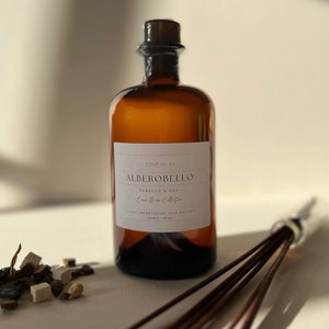 May include: A brown glass bottle with a label that reads "SCENT NO. 04 ALBEROBELLO TABACCO & OAK Casa Bianca Collection LUXURY AROMATHERAPY REED DIFFUSER 500ML / 16.9 OZ".