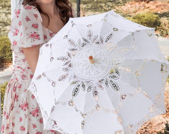 May include: A white lace parasol with a wooden handle. The parasol features intricate floral and geometric patterns. The image shows a close-up of the open parasol, highlighting its delicate design. The parasol is a vintage-inspired accessory.