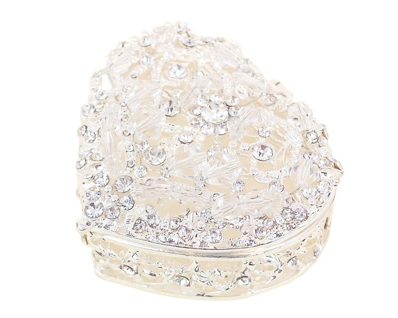May include: A silver heart-shaped trinket box with a decorative design of clear rhinestones.