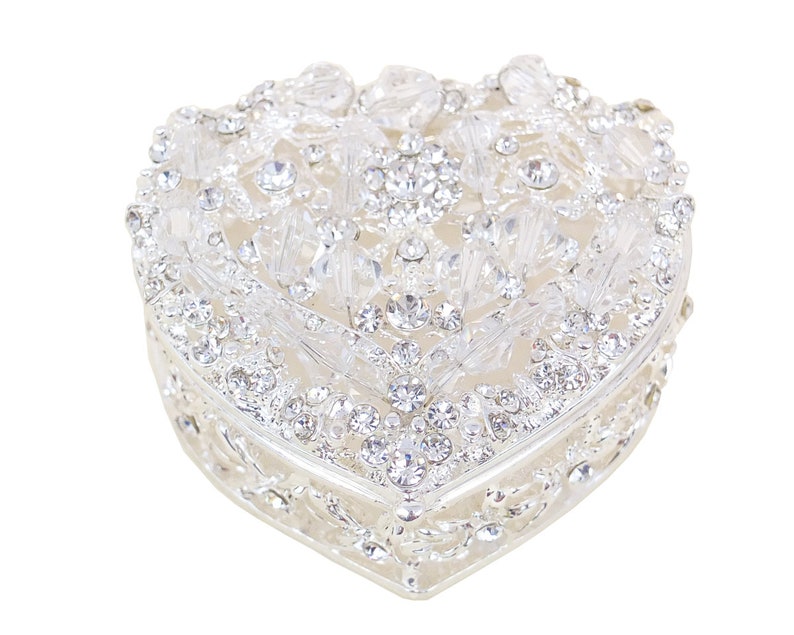 May include: A heart-shaped trinket box with a silver finish and intricate floral design. The box is adorned with clear rhinestones.