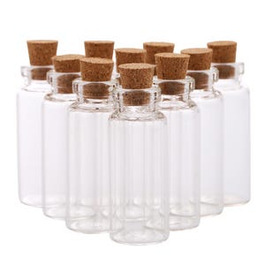 May include: A collection of clear glass bottles with cork stoppers. The bottles are cylindrical and arranged in a triangular formation. The corks are a light brown color, contrasting with the transparent glass.