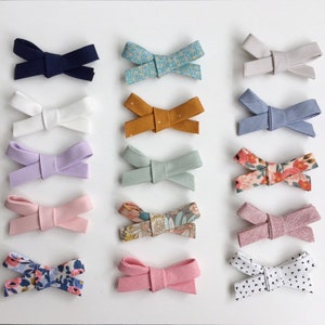 May include: Assortment of 15 fabric hair bows in various colours and patterns, including floral, polka dot, and solid colours. The bows are arranged in three rows of five.