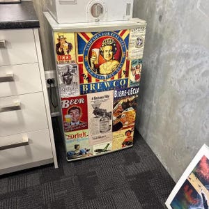 Puede incluir: Un refrigerador compacto cubierto con un collage de anuncios de estilo vintage con tem&aacute;tica de cerveza y pubs. La parte frontal presenta varias ilustraciones, incluido un retrato de una reina y textos que dicen Campaign for Real Ales, Brewco y Beer.