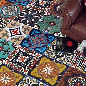 Op de afbeelding: Een kleurrijke tegelvloer met verschillende patronen en kleuren, waaronder blauw, groen, rood, geel en zwart. De tegels zijn in een willekeurig patroon gerangschikt, wat een uniek en opvallend ontwerp creëert. Op de achtergrond is een bruine leren bank te zien, en er liggen een paar vinylplaten op de vloer.