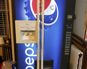 May include: A tall, black Pepsi-branded vending machine featuring a large blue, red, and white bottle cap graphic. The machine includes a beige water dispenser unit on the left door, a vertical selection panel on the right, and white text reading CALORIES COUNT.